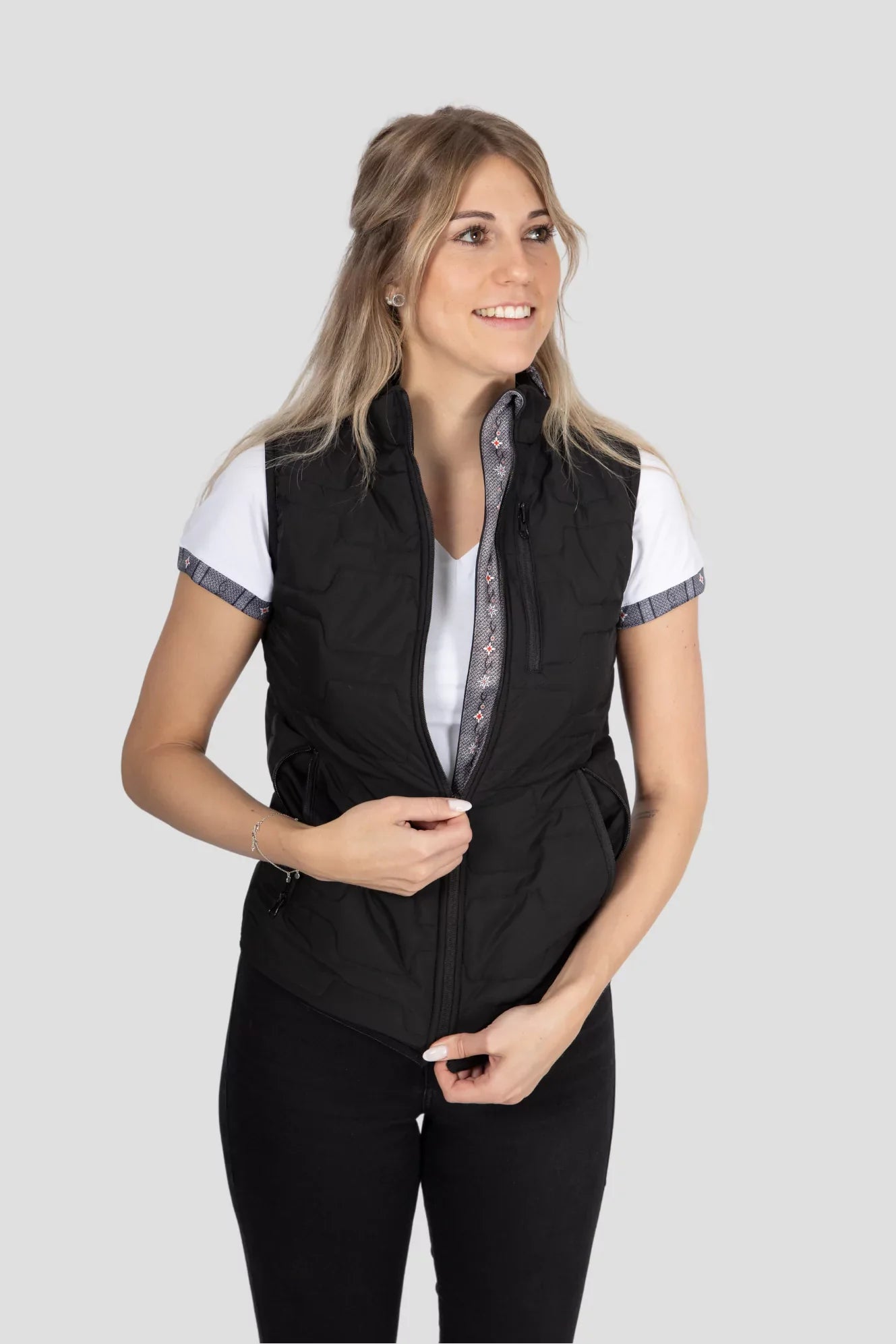 Gilet Edelweiss Damen in Schwarz mit grauem Edelweiss-Muster, hochwertig verarbeitet, mit dezenten Edelweiss-Streifen am Reissverschluss und Nacken, ideal für Freizeit, Arbeit und elegante Anlässe